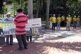 图:中国大陆游客在法轮功真相展板前细看内容(右边是学员每日的晨炼)