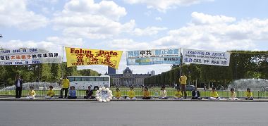 法轮功学员在战神广场上一字排开炼功、发正念,身后是与埃菲尔铁塔遥遥相望的军校(Ecole